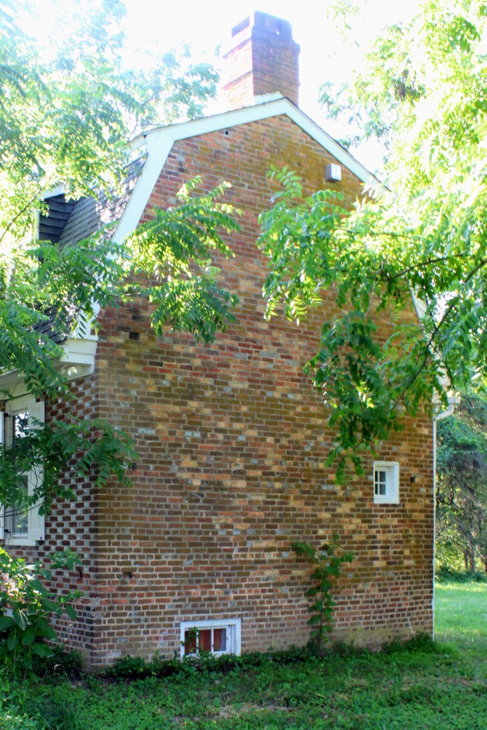 A profile of the eastern gable end, showcasing a solid, utilitarian brick wall designed to withstand the elements. This side features minimal openings, including a tiny accent window on the main floor and a ground-level basement window.
