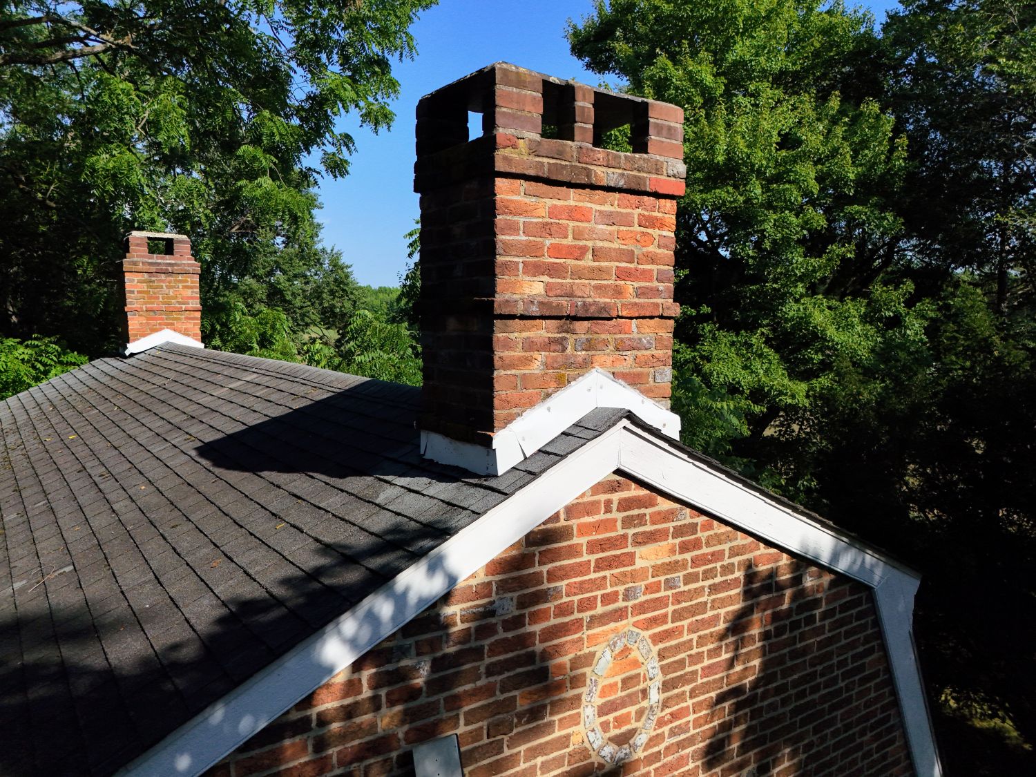 An overhead look at the shingled roofline and one of the home's substantial brick chimneys. Just below the roofline trim, a decorative glazed brick oval is visible on the gable peak, demonstrating the meticulous detail the masons poured into every side of the home.