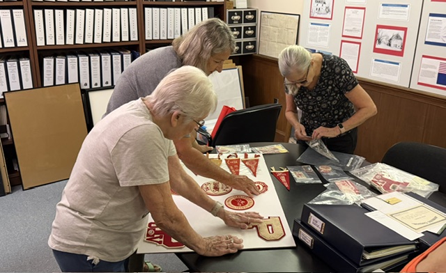 Historical society volunteers arrange a series of Penns Grove High School patches for a display during a recent work session.